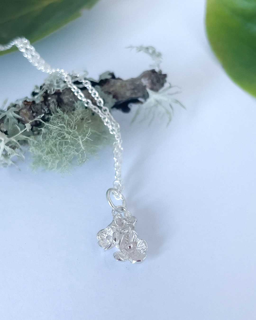 An image of the  Dainty Flower Bouquet of three sterling silver flowers and the Sterling Silver Chain draped over a mossy twig and between green leaves