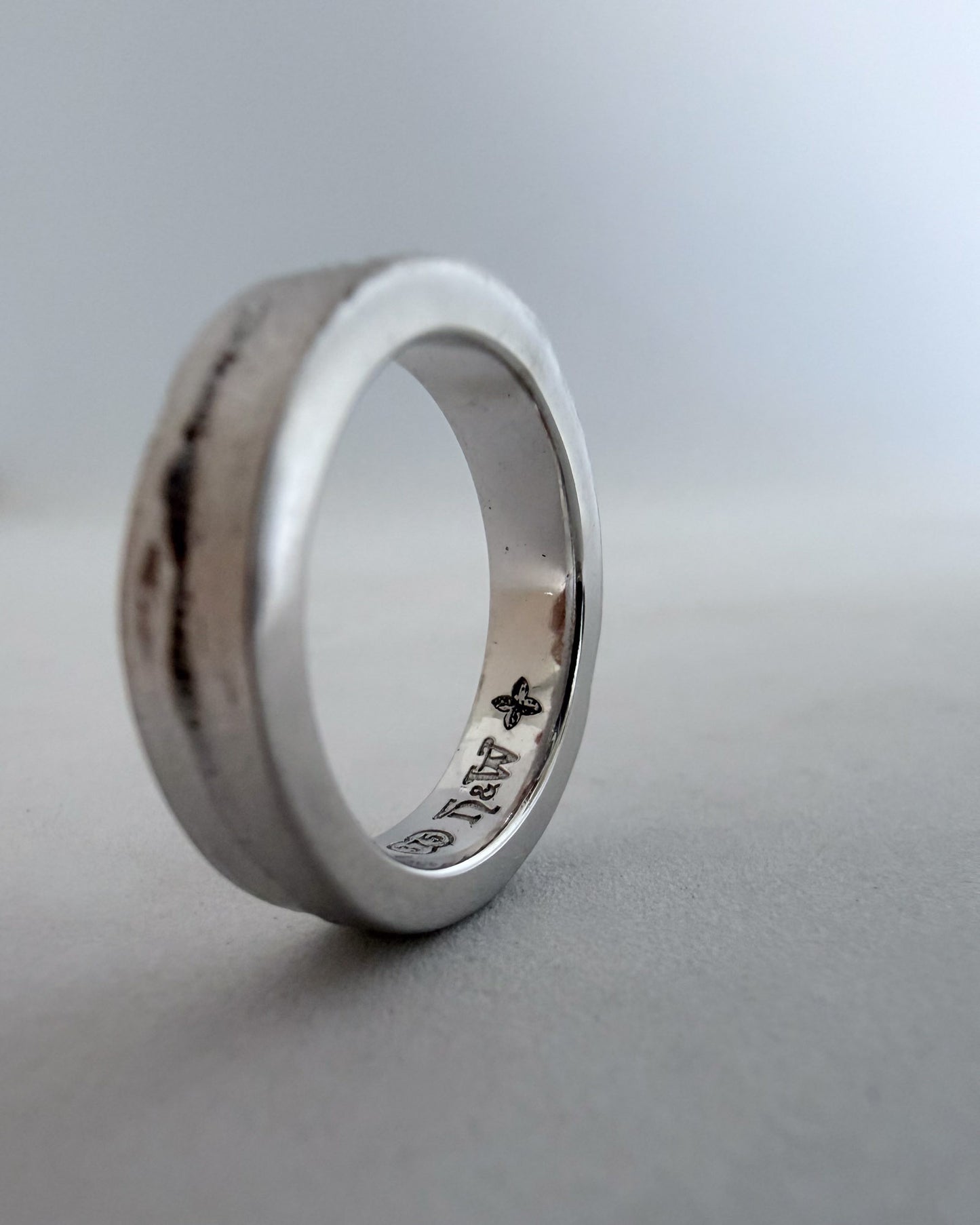 Side angle of the handcrafted white gold sandcast ring, showcasing a custom personalized engraving on the smooth inner band against a blue-grey background.