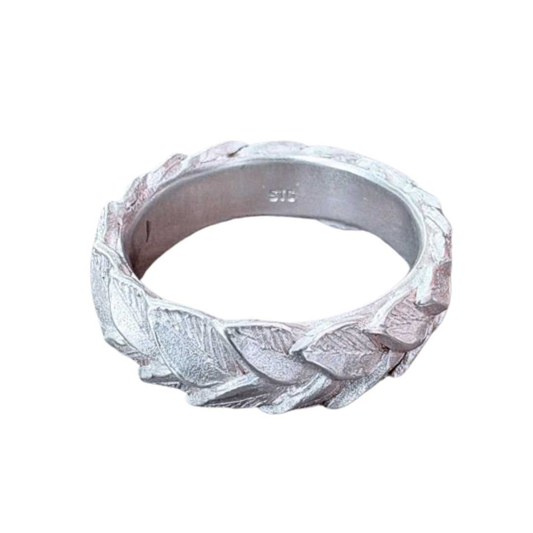 Front view of sculptural sterling silver laurel leaf wedding band on light background, showing dimensional hand-carved leaf details and organic texture