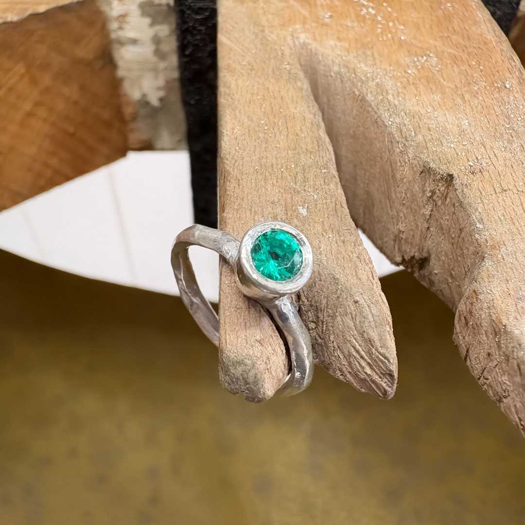 Cherish Ring in sterling silver, Size O, balancing on a jeweller’s bench peg from a top left angle, showing the flush-set Biron emerald.