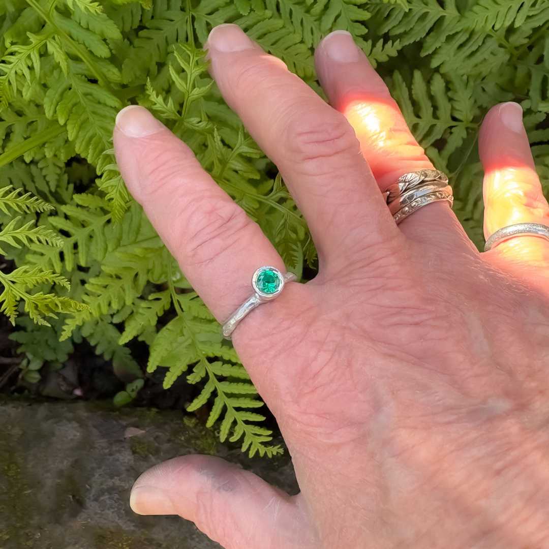 Cherish Ring in sterling silver, Size O, worn on a hand in front of a basalt rock and green ferns, with artistic lighting highlighting the hand.