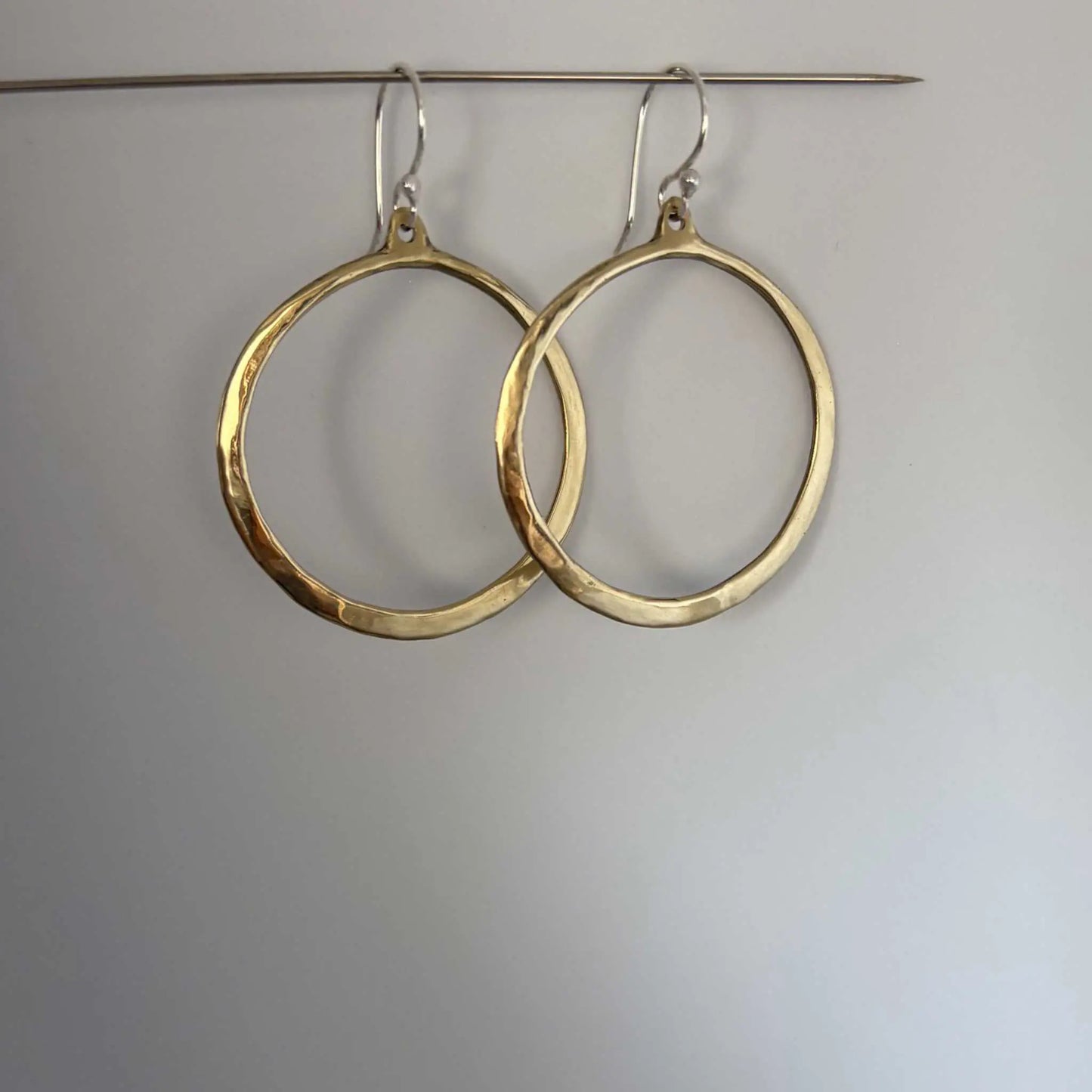 Lunar Eclipse hoop earrings in polished golden bronze with sterling silver hooks, hanging from a silver wire with soft shadows on a graduated grey background