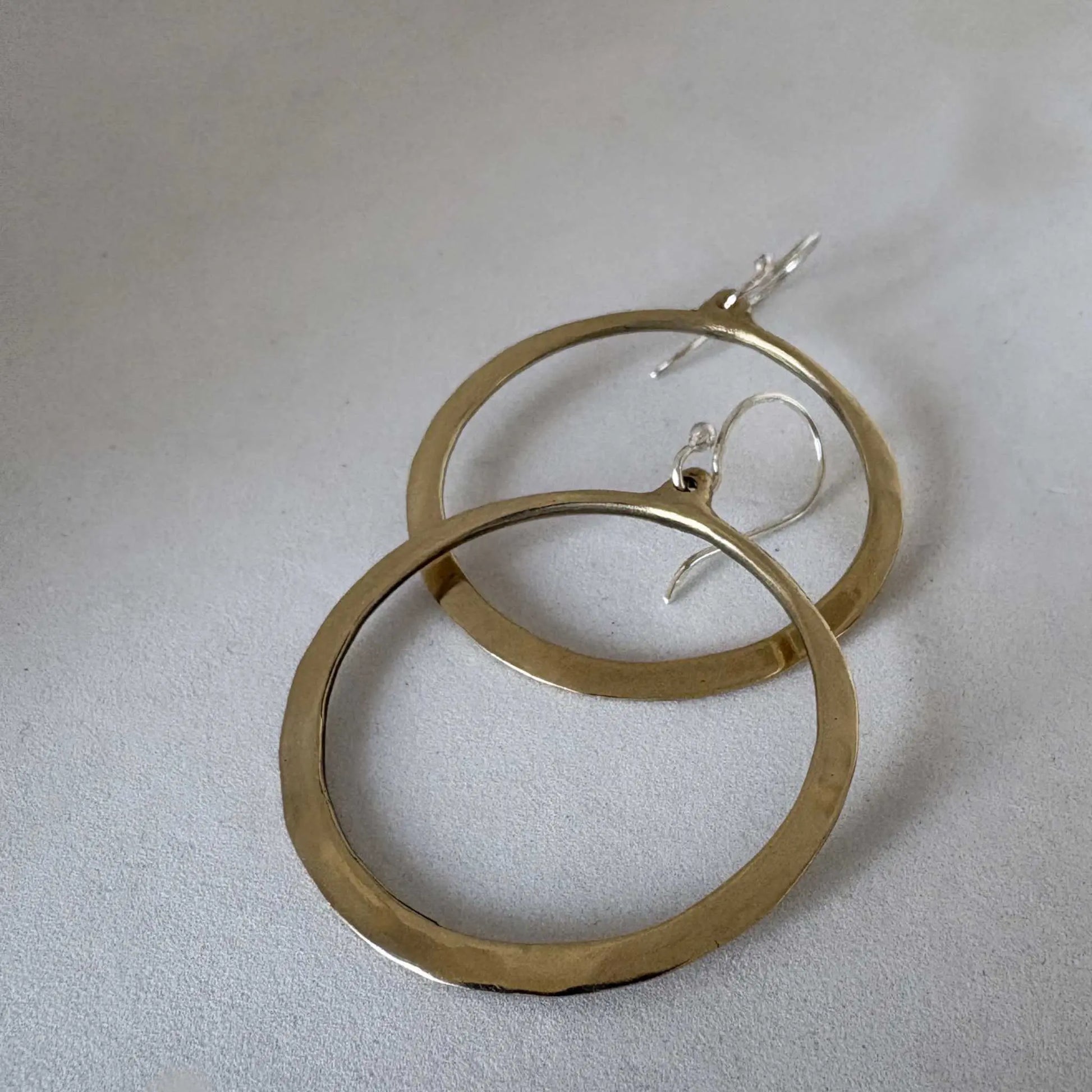 Lunar Eclipse hoop earrings in polished golden bronze with sterling silver hooks, lying in a line overlapping and viewed from a slight top right angle