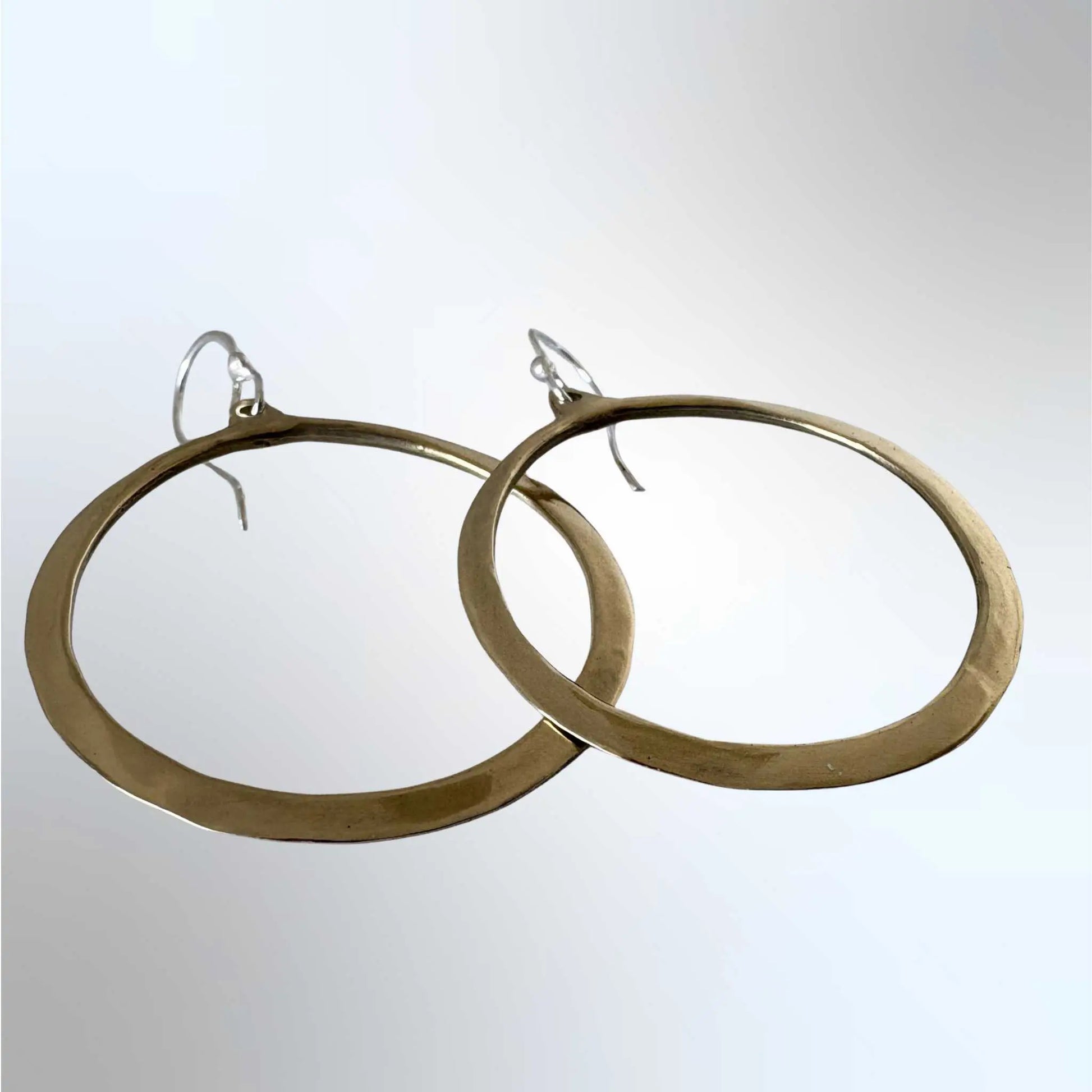 Front view of Lunar Eclipse hoop earrings in polished golden bronze with sterling silver hooks, slightly overlapping on very light grey background