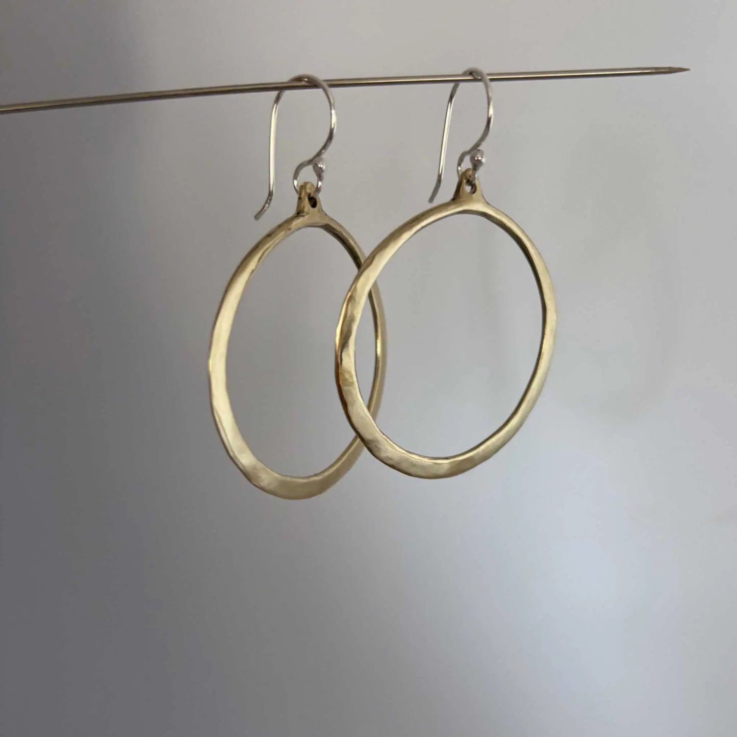 Lunar Eclipse hoop earrings in polished golden bronze with sterling silver hooks, hanging from a silver wire showing a slight side profile against a grey background