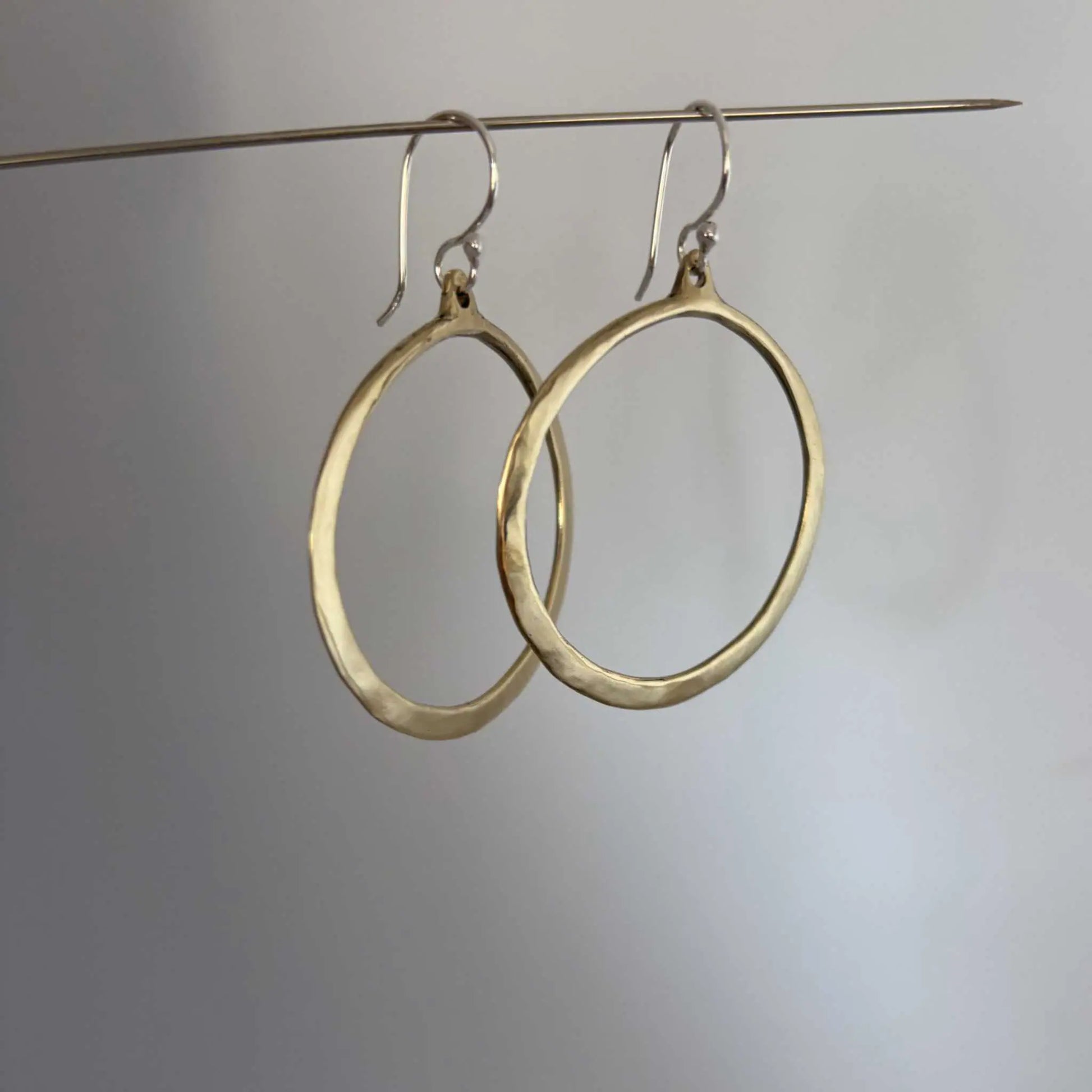 Lunar Eclipse hoop earrings in polished golden bronze with sterling silver hooks, hanging from a silver wire showing a slight side profile against a grey background