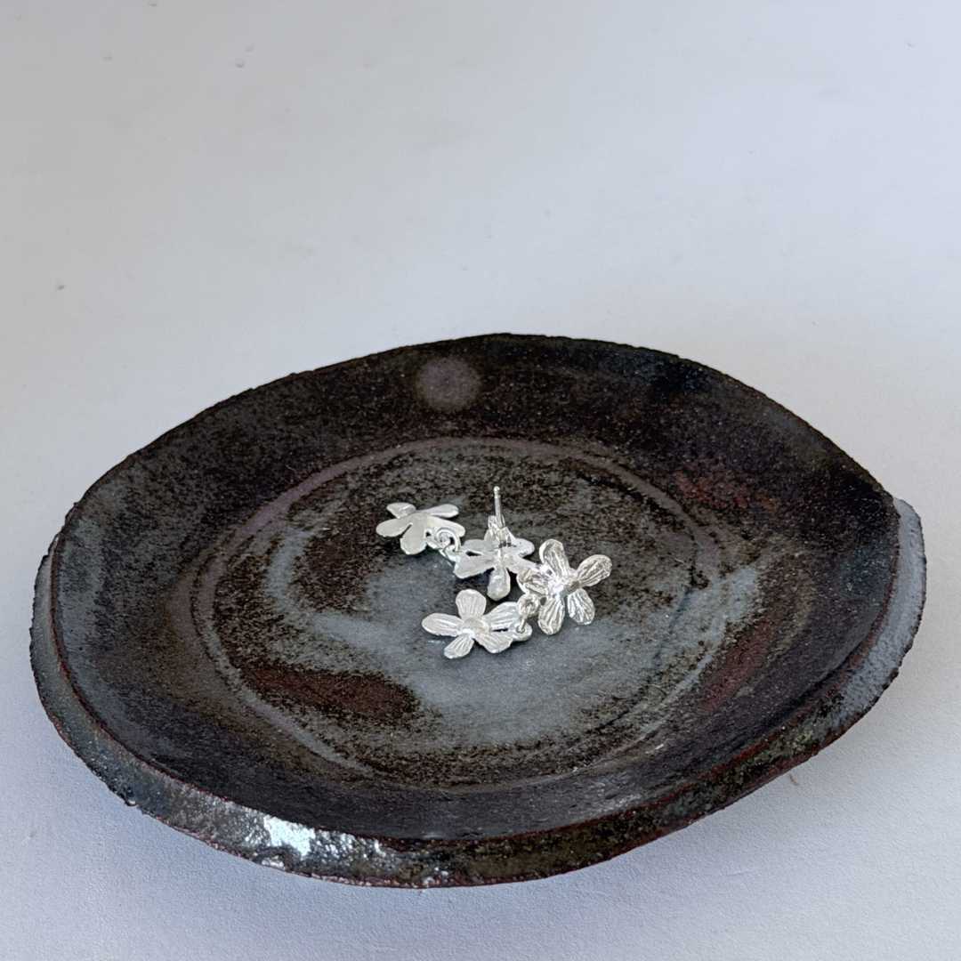 Flora Duo Drop Stud Earrings in sterling silver resting in a ceramic pottery dish, positioned to show the back of the earring including the post and butterfly back fastening.
