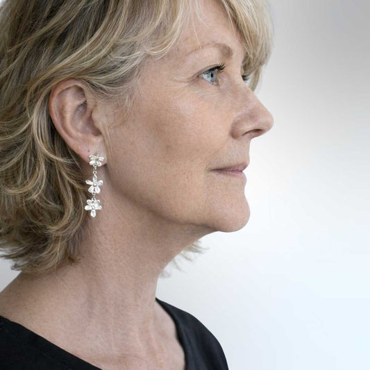 Woman wearing Flora Trailing Flower Earrings showing 45mm length and three cascading sterling silver flowers - side profile view of botanical drop earrings perfect for day to evening wear