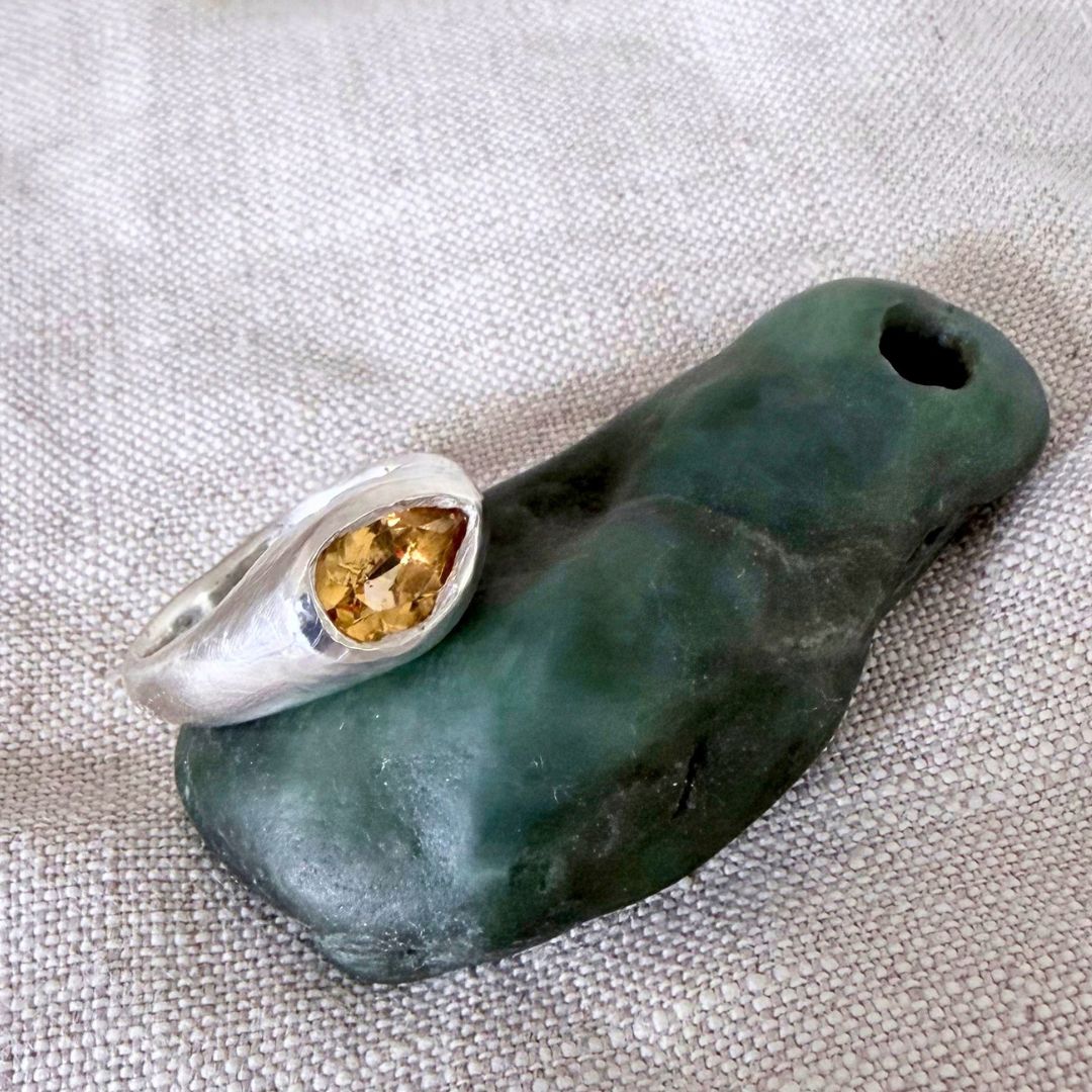 Side view of Kōwhai Signet Ring showing the sculptural sterling silver profile and natural citrine beside pounamu