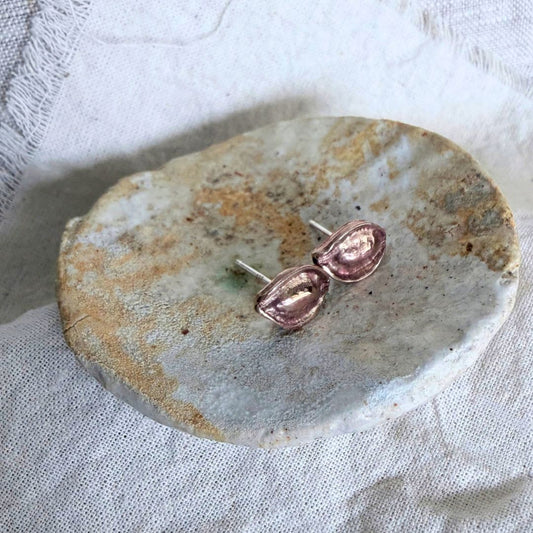 Bronze Kōwhai Pod stud earrings with sterling silver posts displayed on a pale stone dish and linen background.