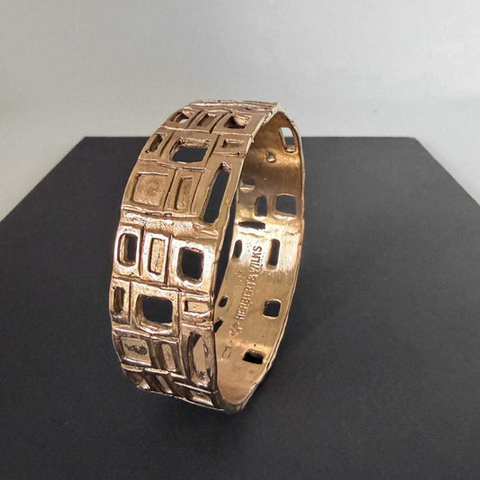 Close-up detail of the cast, organic texture and hallmark branding inside the HerbertandWilks Modernist Bangle, finished in warm, caramel-toned bronze against a dark grey and black background.