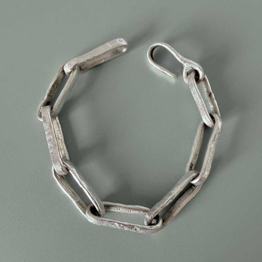 Heavy sterling silver paperclip chain bracelet on green textured surface with directional shadow – handmade in Auckland NZ