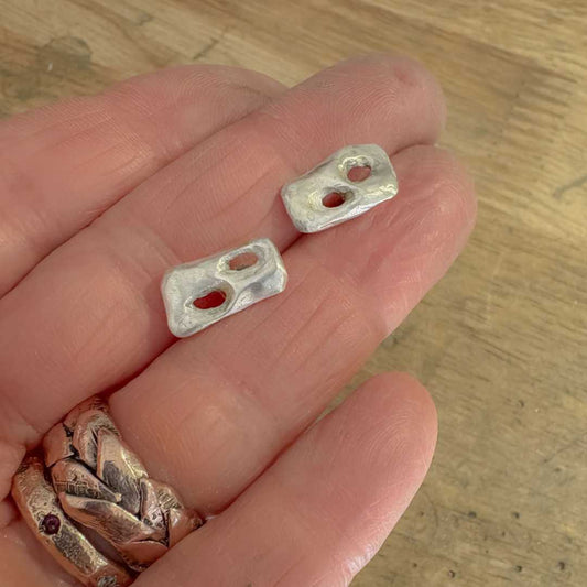 Sterling silver Perfora Rectangle Stud Earrings displayed face up on a hand, set against a wooden surface, highlighting pierced rectangular design.