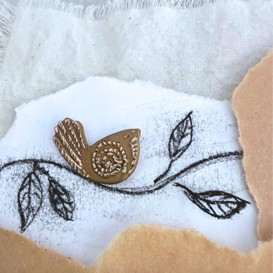 Bronze Pīwakawaka Fantail Pin beside hand-drawn leaves and branch