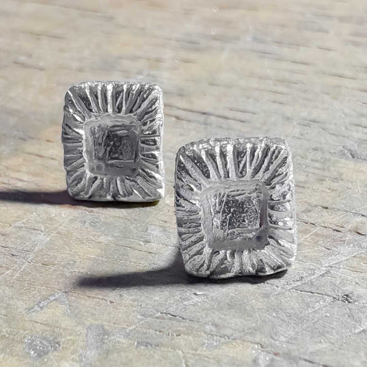 Sterling silver Strata Rectangle Stud Earrings resting on a wooden workbench after making, showing textured frame and smoother centre.