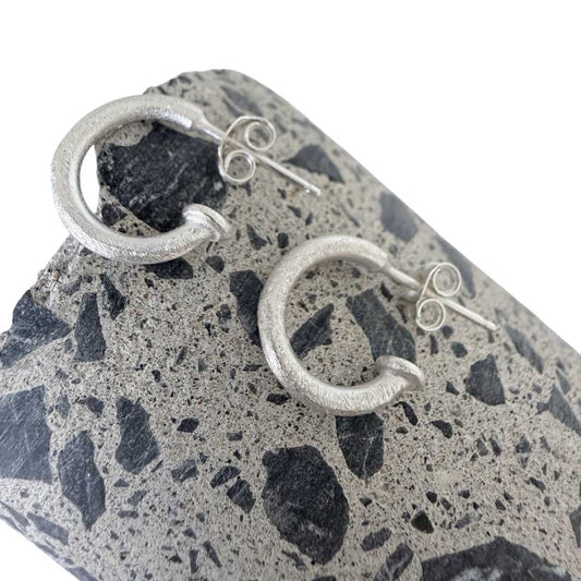 13mm textured sterling silver hoop earrings lying on cut concrete surface showing stone chip detail viewed from above
