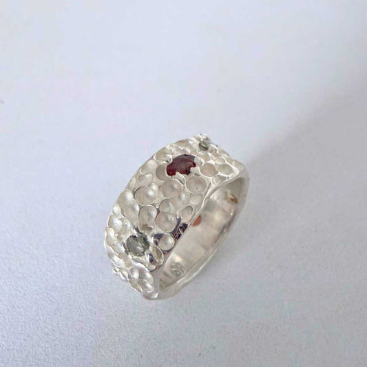 Trace Ring in sterling silver standing on edge with textured crater surface and seven sapphires, sculptural shadow detail