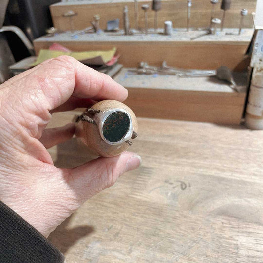 Bloodstone Signet Ring in silver held in a ring clamp on workbench, shown just after being set, highlighting handcrafted jewellery process – HerbertandWilks Jewellery”