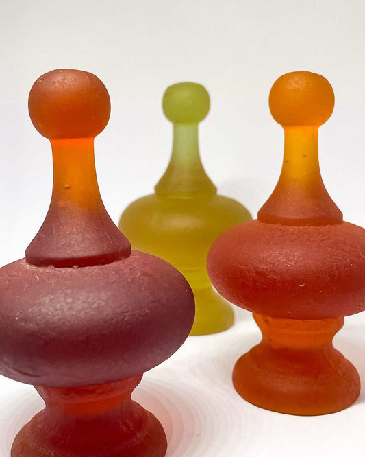 A dark orange and an orange cast glass finial are standing in front of a rhubarb finial