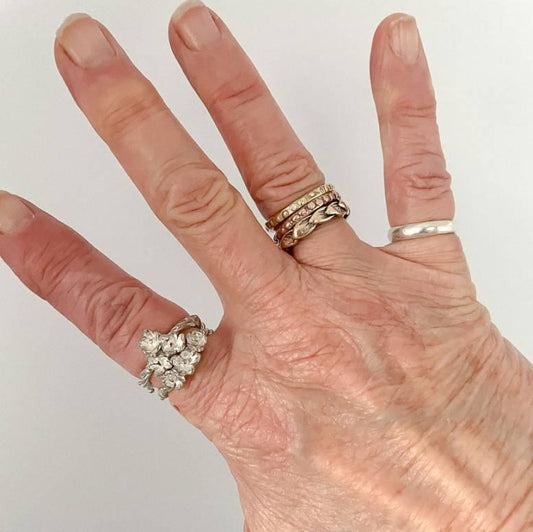 Threaded Bloom Ring worn on the hand, stacked with another floral ring. Sculpted silver flowers and fine vine details are visible against the skin
