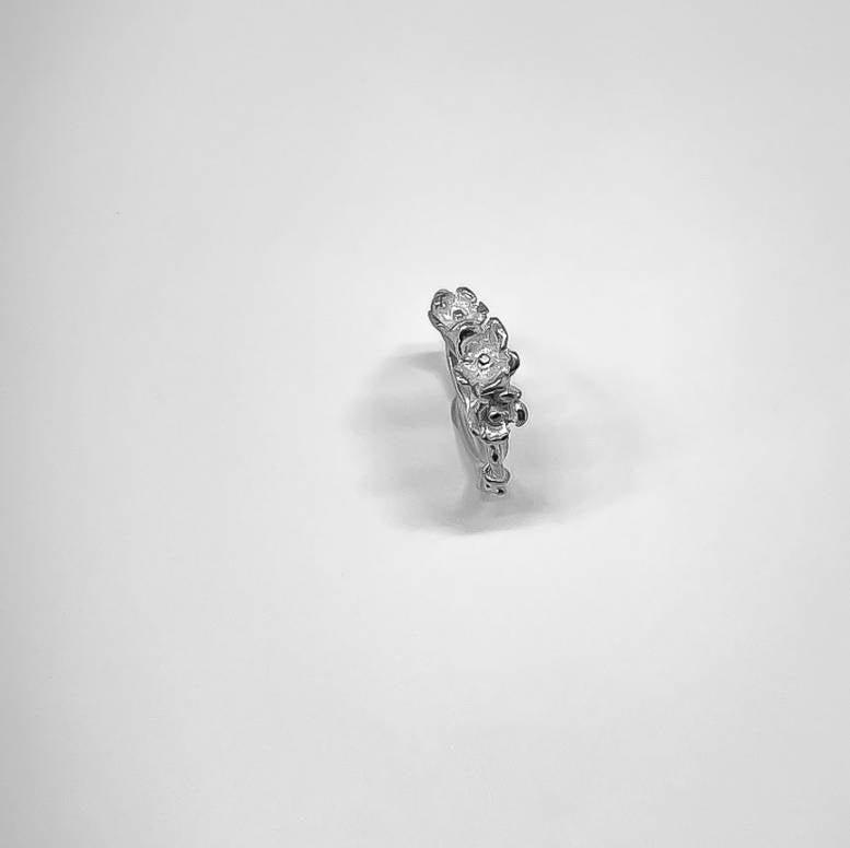 Threaded Bloom Ring standing upright on a white surface, viewed from a slight downward angle to show sculpted flowers and entwined vine detail