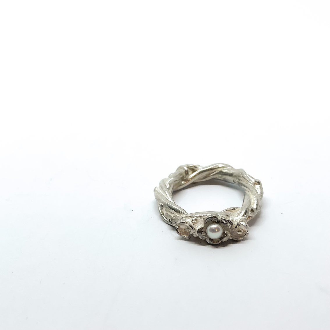 Sterling silver Interwoven Flower Ring with a central freshwater pearl, lying on its right side at the front on a white background.