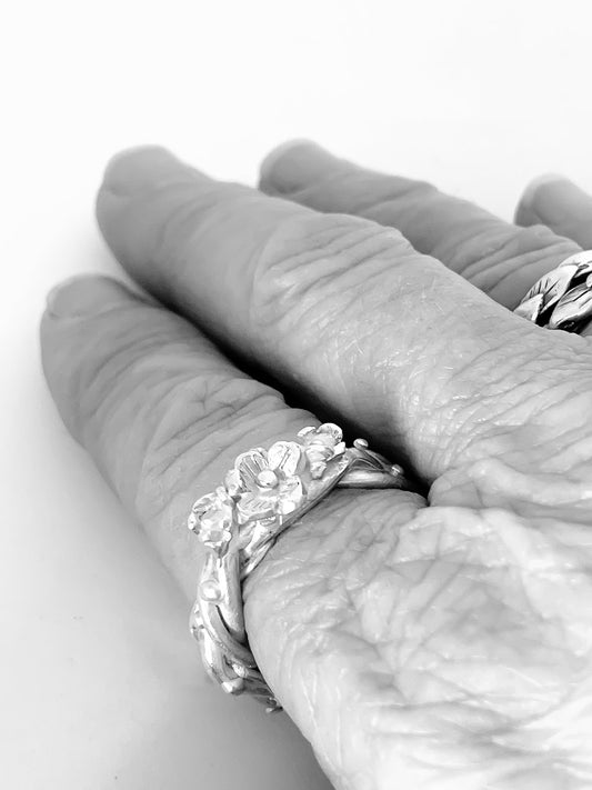 Sterling silver Interwoven Flower Ring with three sculptural blossoms, shown being worn on the hand as a bold botanical statement piece.
