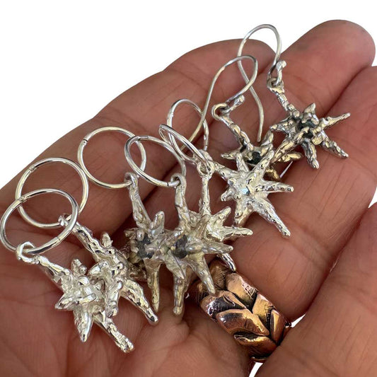 Hand-forged sterling silver faerie star charms balanced on hand showing seven-pointed star detail and natural texture