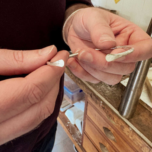 Close-up of hands holding a finished sterling silver cuff beside a jewellery workbench after the Maker Cuff Workshop in Mt Eden, Auckland
