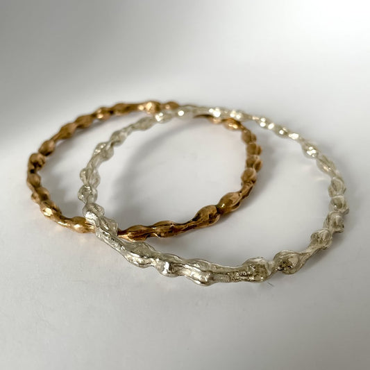 Silver and bronze kōwhai bangles stacked together on light grey surface