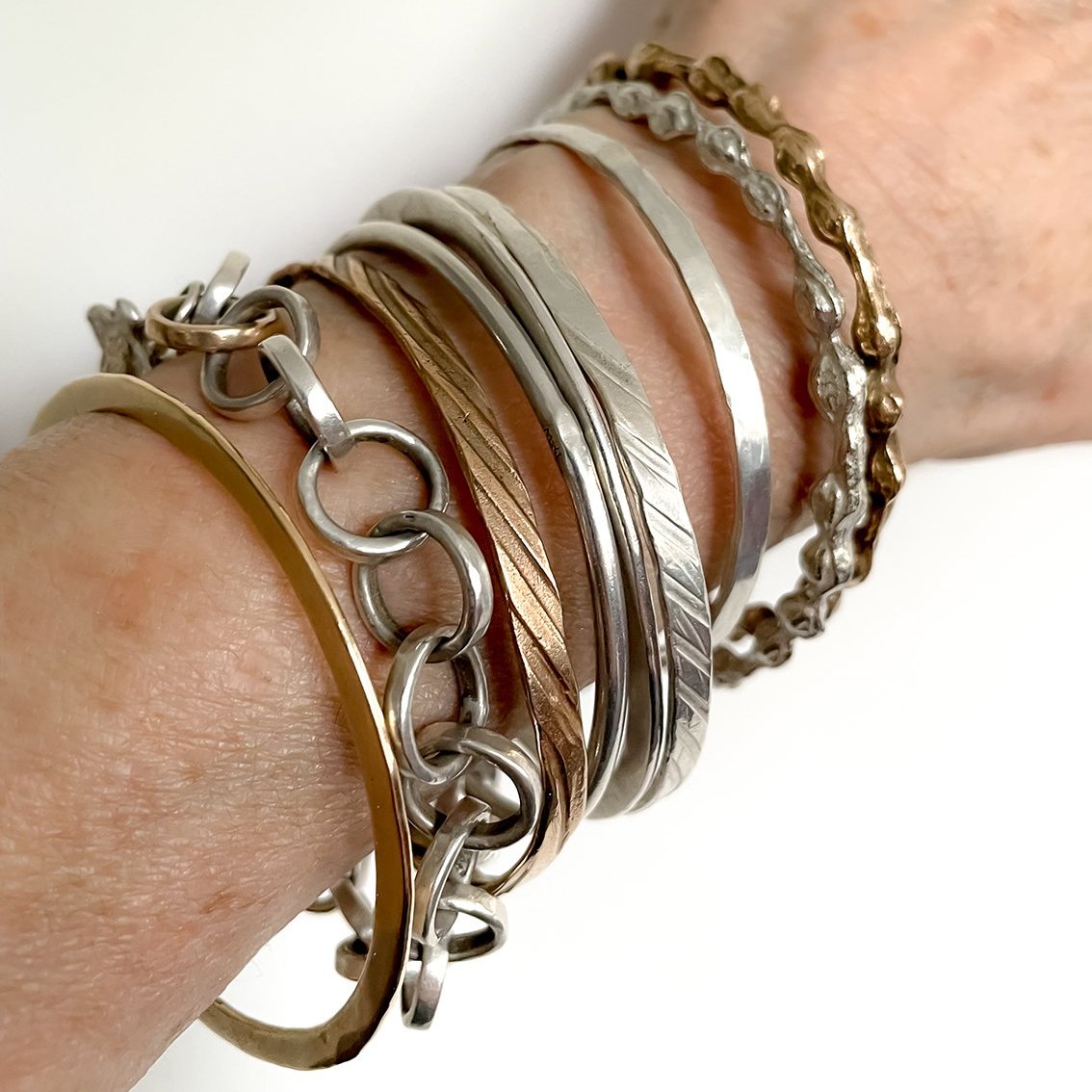 Bronze bangle worn stacked with other warm-and cool toned jewellery in soft light