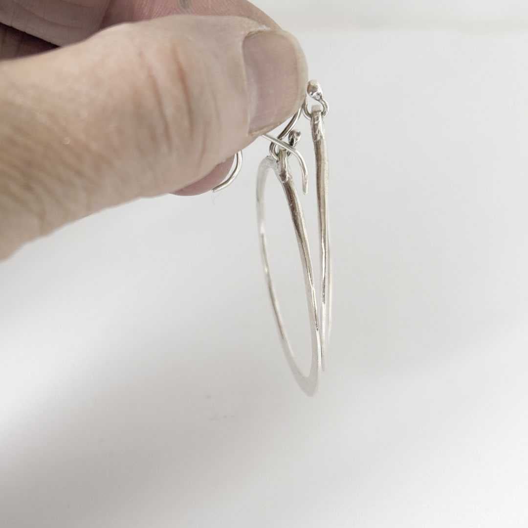 Lunar Eclipse Hoop Earrings in sterling silver being held to show the fine knife edge tapering at the base of the hoop
