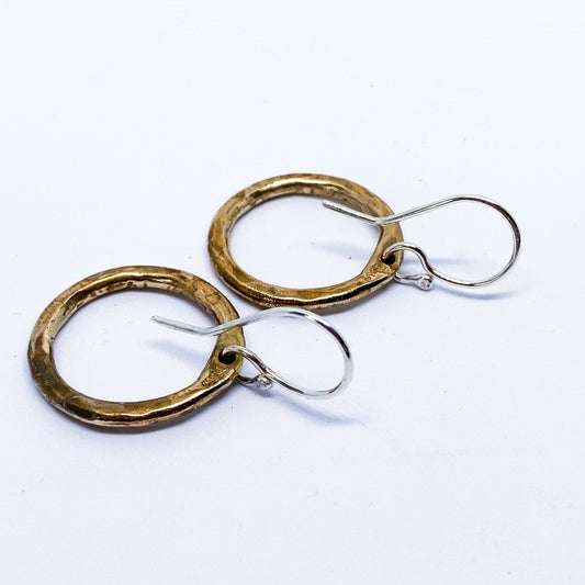 Close-up of mixed-metal hoop earrings lying face down showing softly curved sterling silver ear hooks and bronze circle