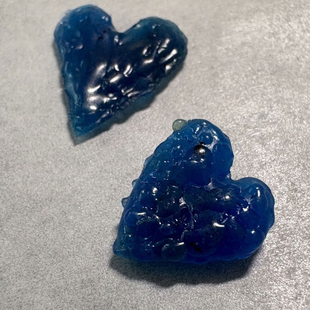 Close-up of two organic textured charms with layered wax build-up showing the different surfaces
