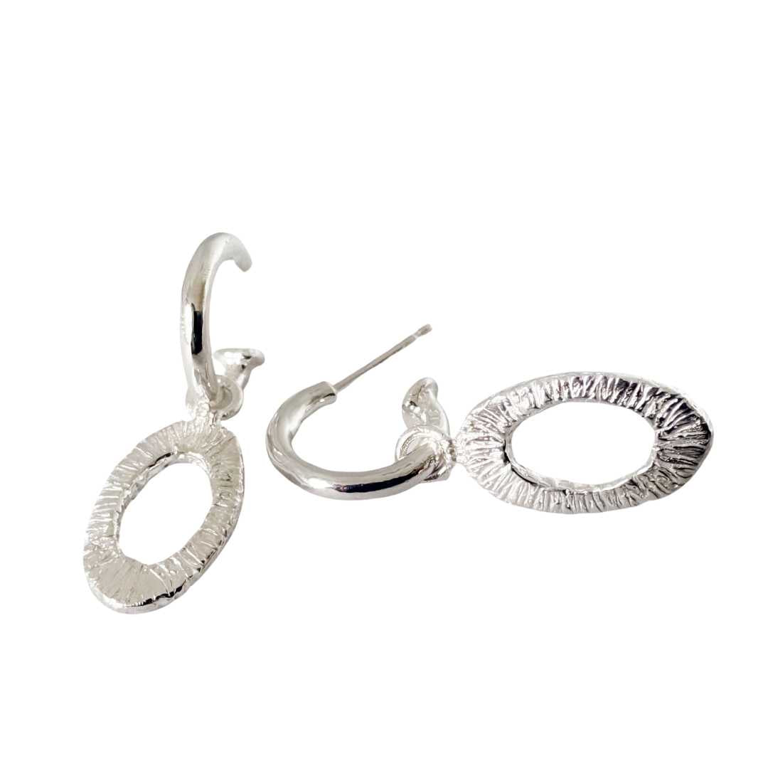 Sterling silver Oval Strata Charm Earrings shown front on and side on, with textured open oval charms hanging from polished silver hoops against a white background.