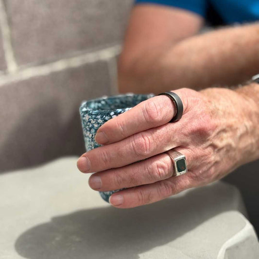 Man wearing Rectangle Bloodstone Signet Ring reaching for a hand-blown glass outdoors, showing the ring’s soft polish and classic silver design.
