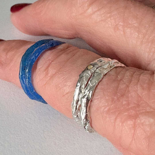 Two sterling silver stacking rings worn on hand alongside blue wax rings showing before and after casting process