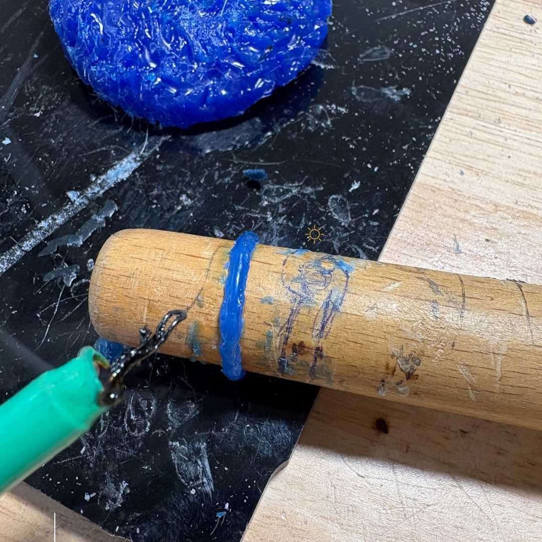 Blue wax ring on wooden mandrel with wax block and heated wax pen tool showing build-up technique