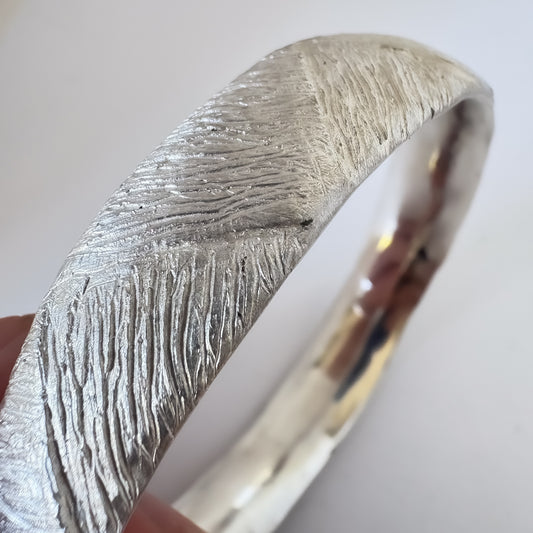 Close-up of the Strata Silver Bangle held against a light grey background — showing the hand-carved woven surface texture and sculptural detail by HerbertandWilks.