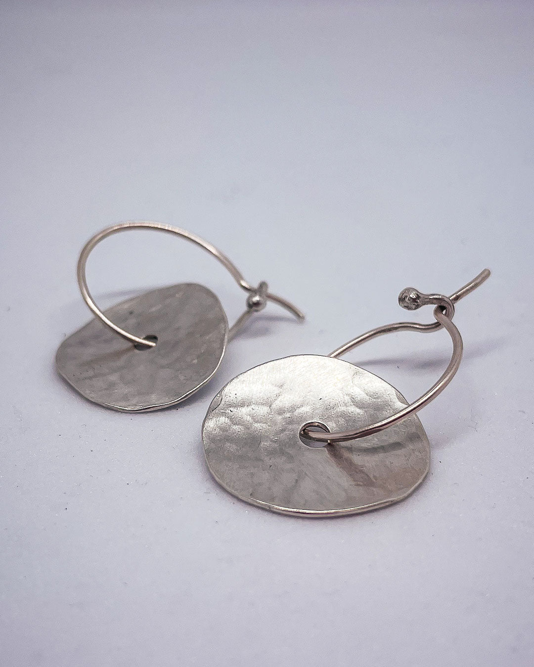 A closeup of a pair of discs of Sterling Silver that sits on a hoop earring