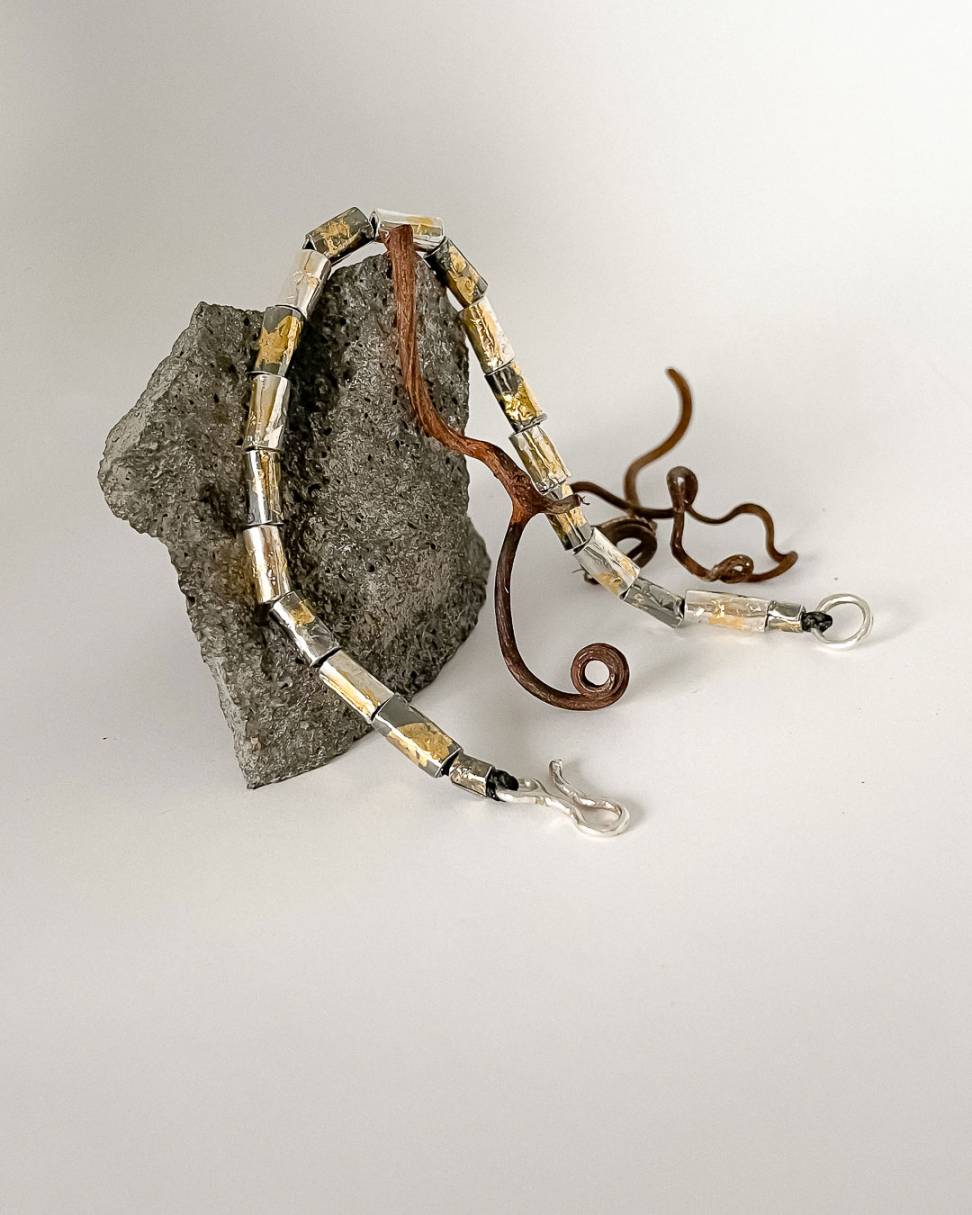 A beaded bracelet alternating between oxidised and plain silver decorated with 24ct Gold Leaf draped over a volcanic rock