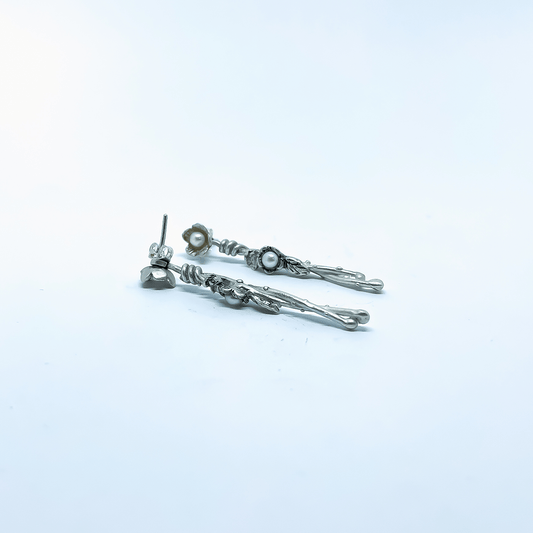 Close-up of Interwoven Flower Earrings in sterling silver with pearl centres, arranged on a pale blue background.