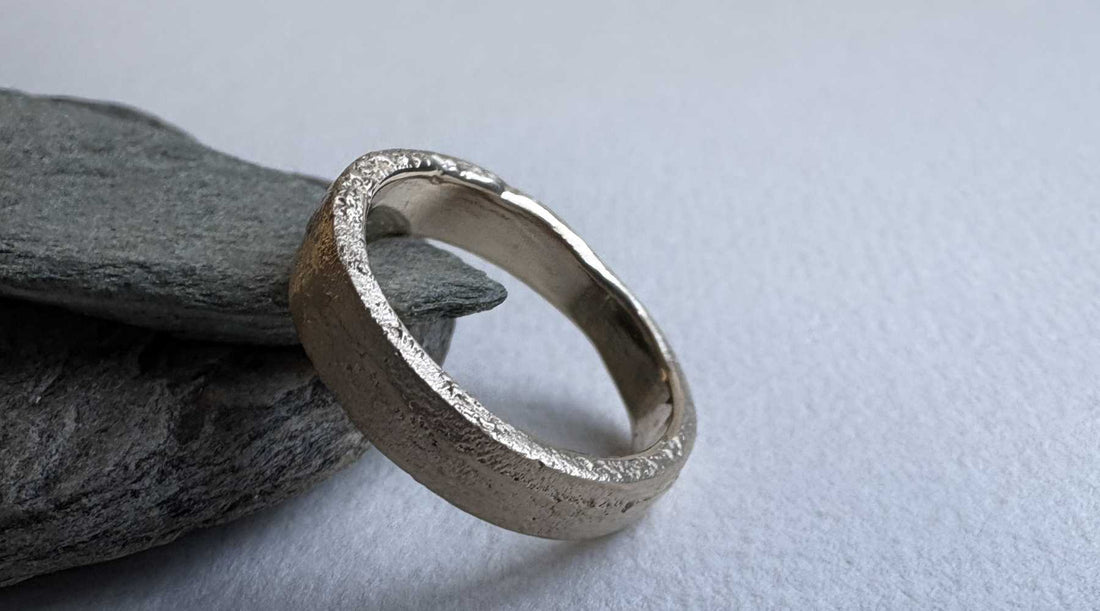 4mm Sandcast Ring – Flat Face in 9ct Yellow Gold leaning against natural rocks, showing both the organic textured outer surface and smooth inner band — HerbertandWilks Jewellery