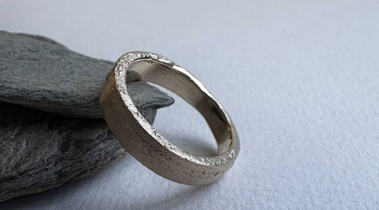 4mm Sandcast Ring – Flat Face in 9ct Yellow Gold leaning against natural rocks, showing both the organic textured outer surface and smooth inner band — HerbertandWilks Jewellery