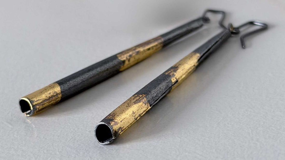 A pair of Keum-Boo Tapered column Earrings in oxidised silver and 24ct gold lying on a light grey textured paper