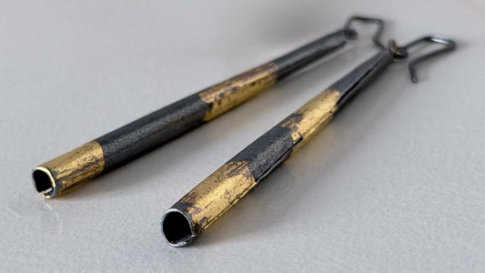 A pair of Keum-Boo Tapered column Earrings in oxidised silver and 24ct gold lying on a light grey textured paper