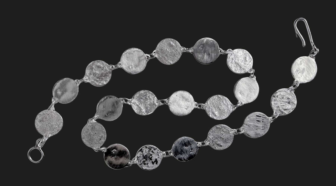 HerbertandWilks Jewellery sterling silver Sequin necklace on a dark charcoal background, displaying the various handcrafted textures on the discs.
