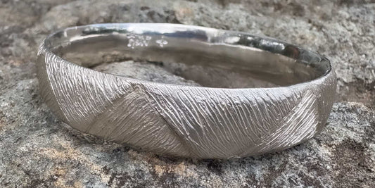 Close-up of the Strata bangle resting on a rock, showing fine hand-carved texture in silver tones