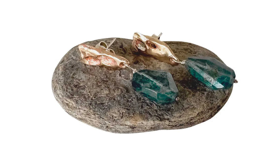 Bronze Perfora Topaz Stud Earrings lying on a textured river stone, designed as a meaningful 8th or 19th wedding anniversary gift.