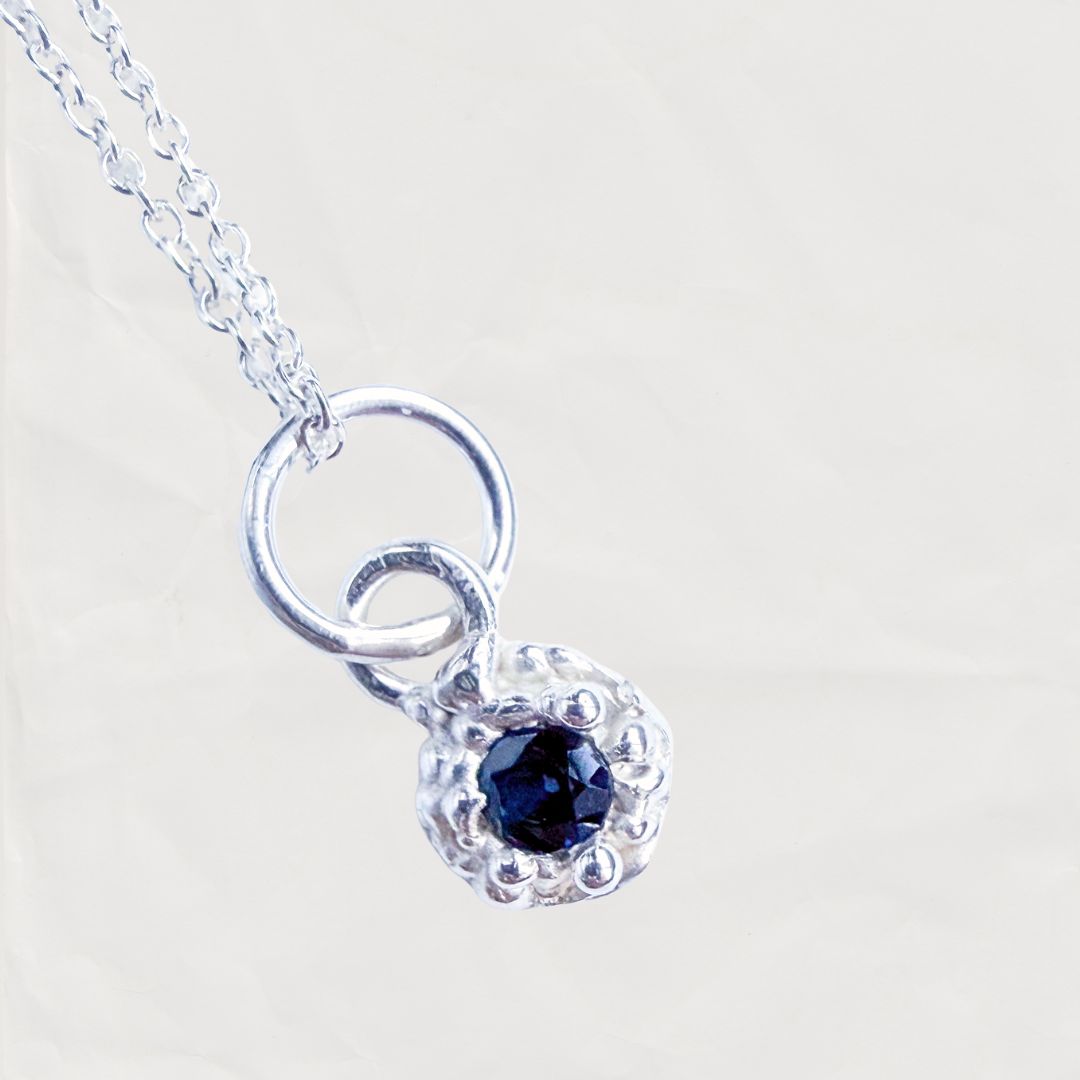 Fluid Dewdrop sterling silver pendant necklace displaying a 3mm natural blue sapphire on a fine cable chain, set against a plain neutral background.